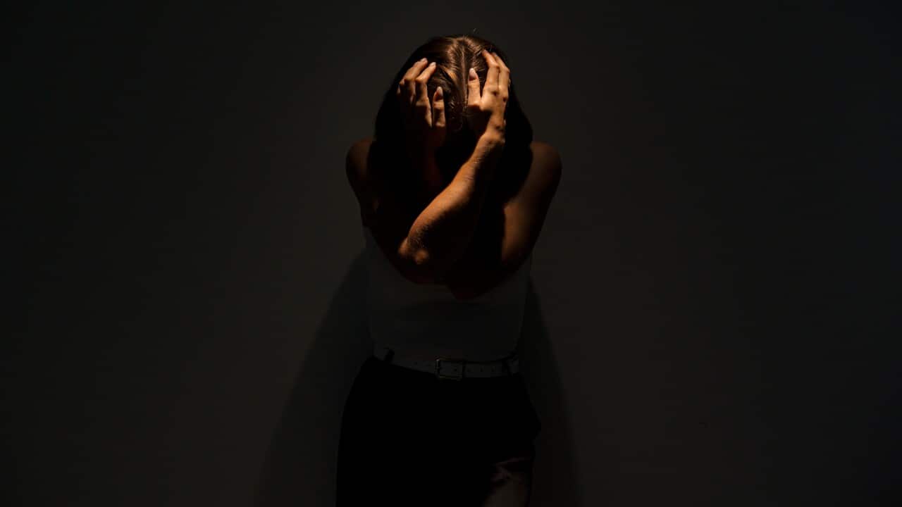 Depressed woman standing in darkness clutching her head in mental anguish.