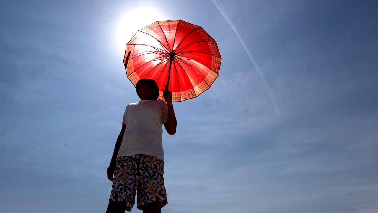 A man walks with an umbrella at Henley Beach during hot weather in Adelaide.