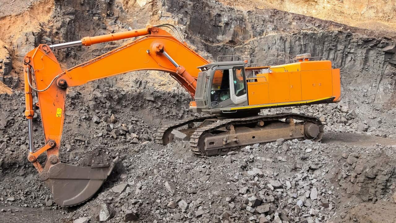 Yellow excavator digging for ore rich rock in an open pit mine