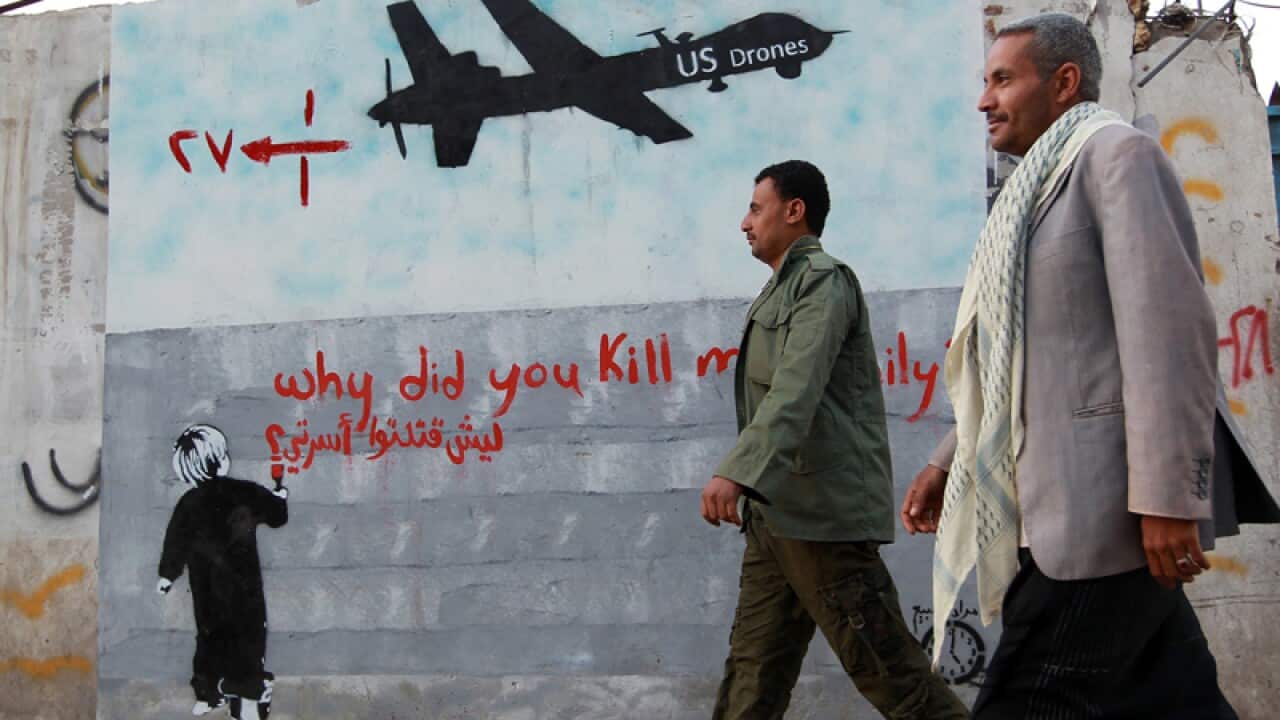 Yemeni men walk past a mural depicting a US drone