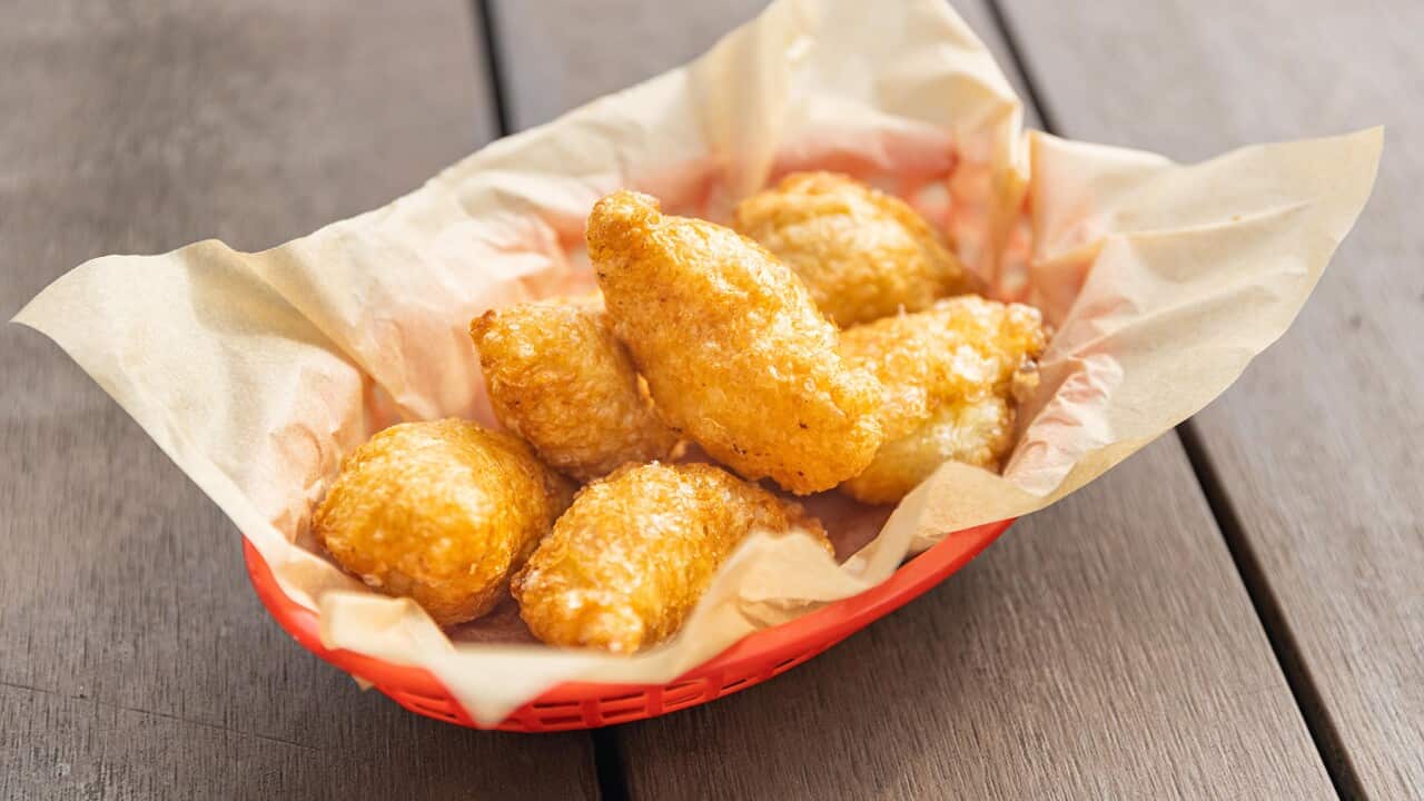 A red plastic basket lined with paper holds six golden curry puffs.