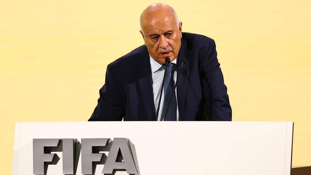 A man in a suit stands at a podium with the FIFA label