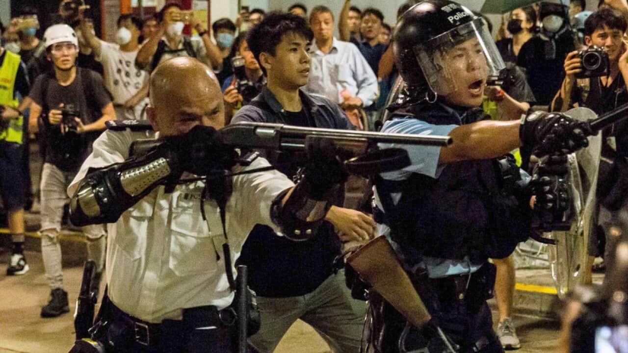 The officer in Kwai Chung points his gun, loaded with beanbag rounds, at the protesting crowd.