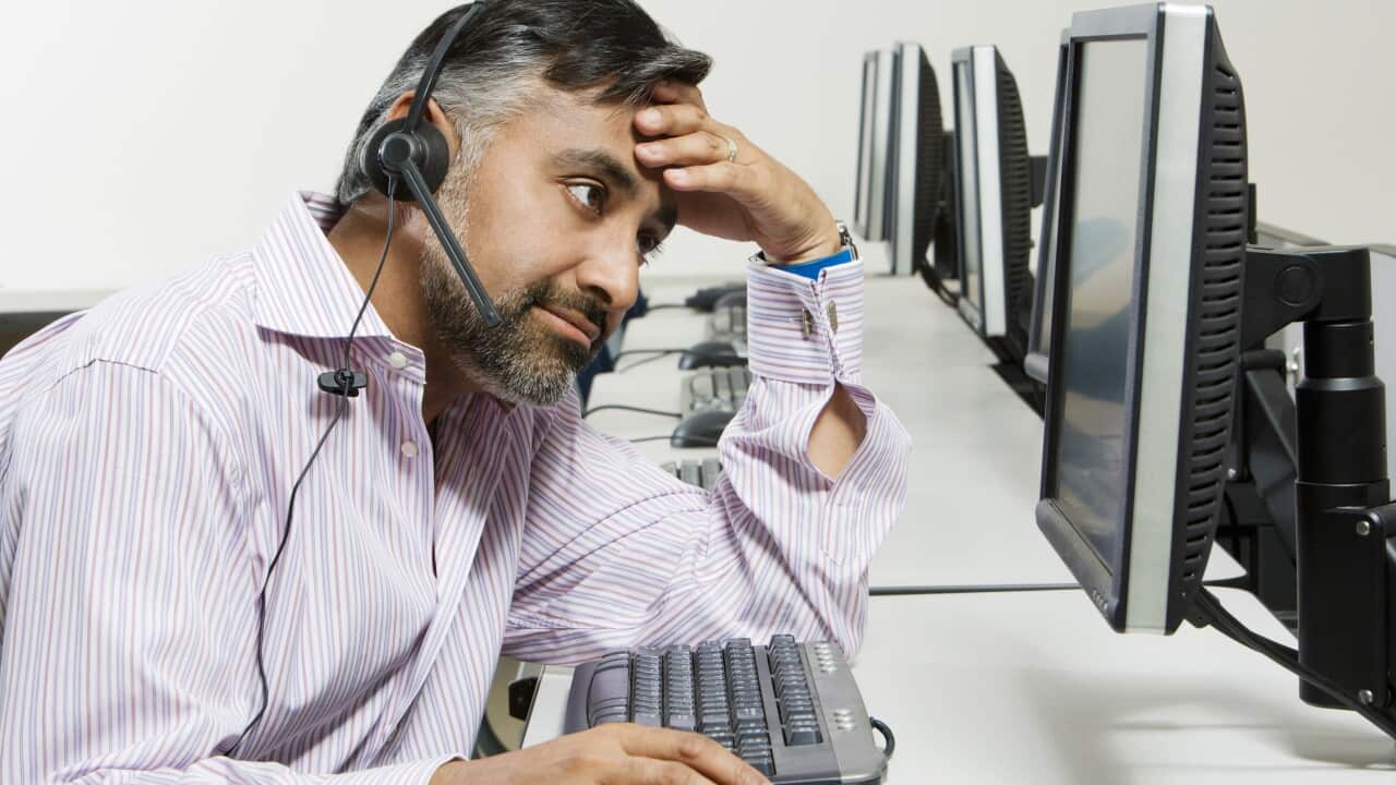 A frazzled-looking man wearing a microphone headset in front of a desktop computer.