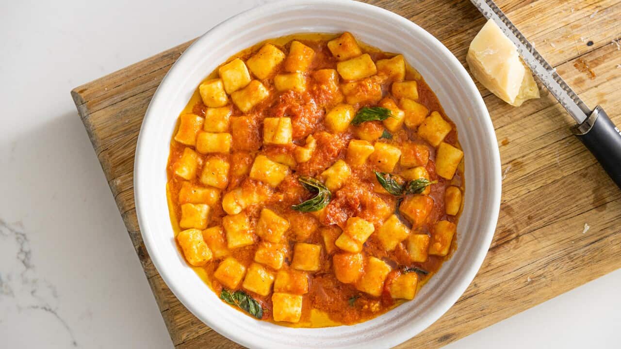 A white bowl sitting on a wooden board holds gnocchi in a tomato sauce.