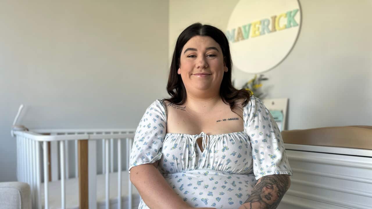 A woman sitting down in a nursery and smiling.