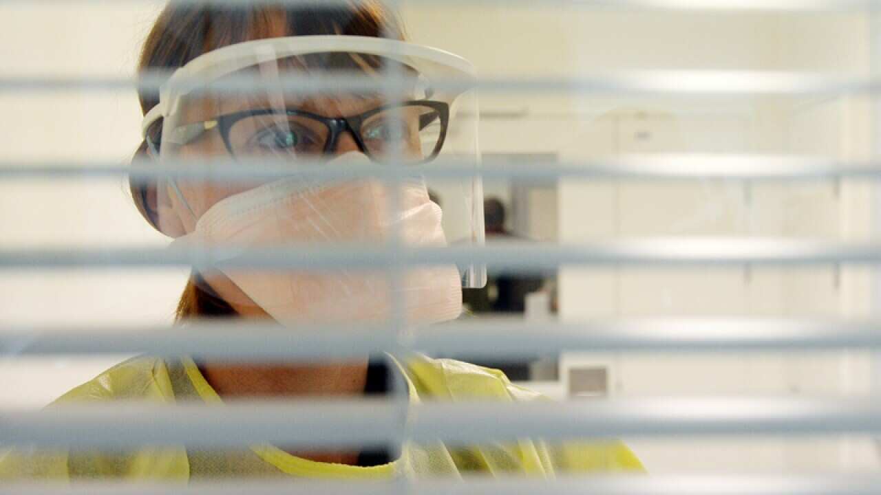A nurse in protective gear looks into an isolation room