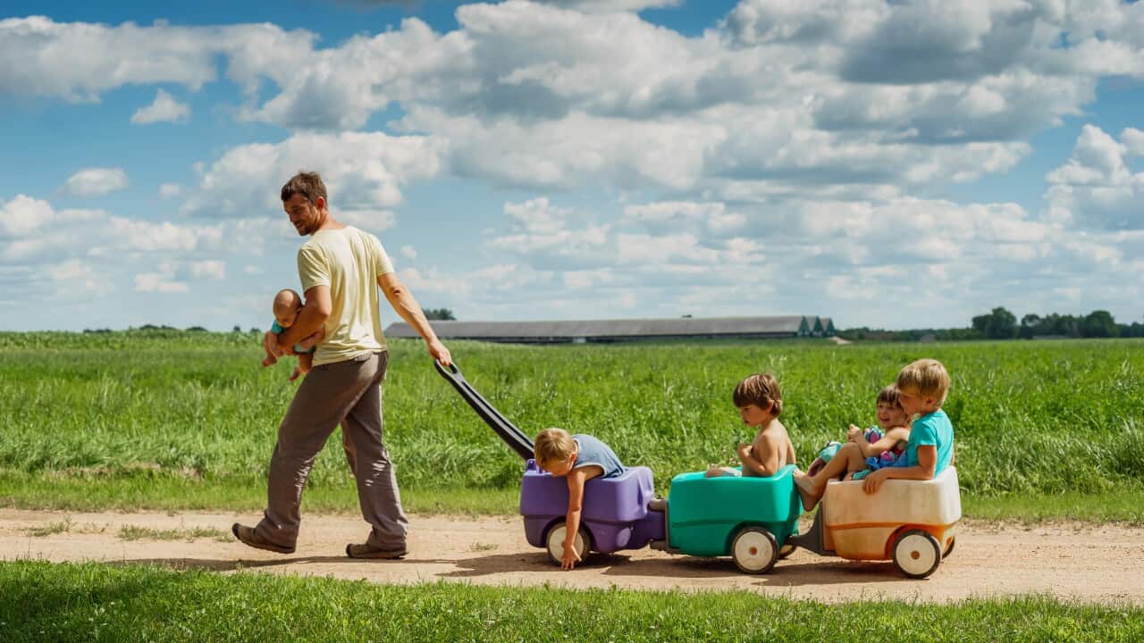 Father carrying baby son while pulling four children in a wagon