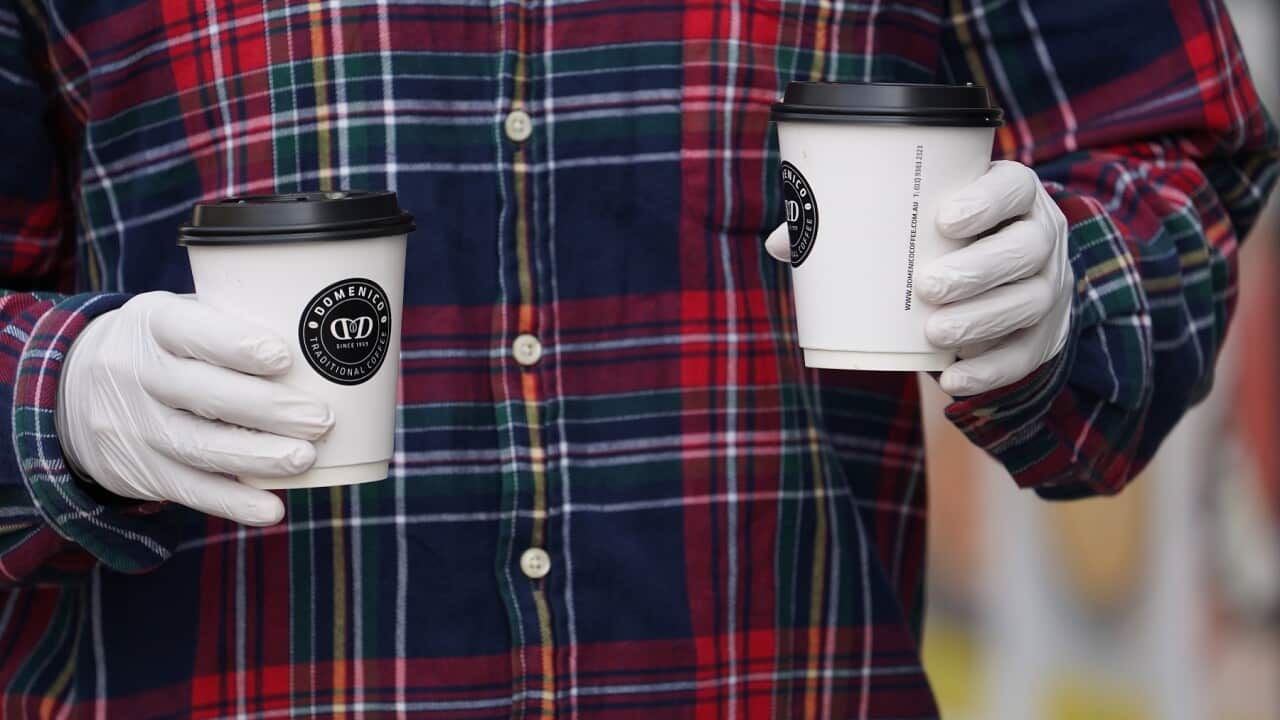 A man holds coffee cups while wearing gloves