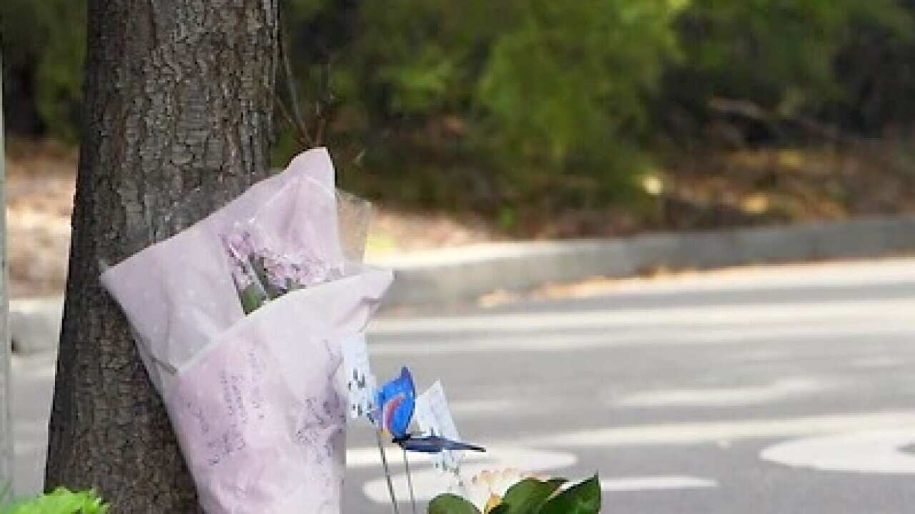 A security guard stands in the driveway as flowers are seen left at the entrance to Anglicare Newmarch House aged care home.