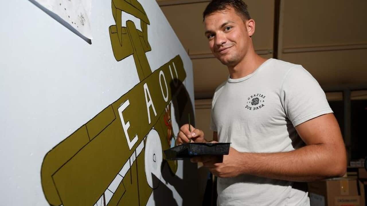 Michal Samoraj poses for a photo while painting a concrete T-Wall.