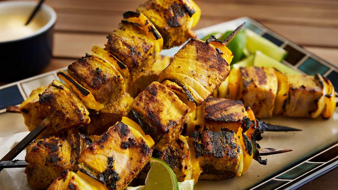 Five skewers, threaded with golden-coloured grilled tuna and onion, sit on a plate with lime wedges.