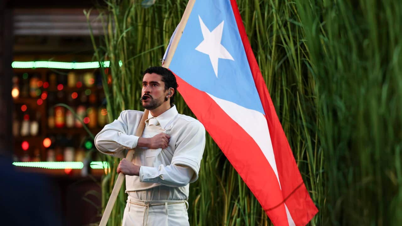 A man holding a Puerto Rican flag in front of long grass.