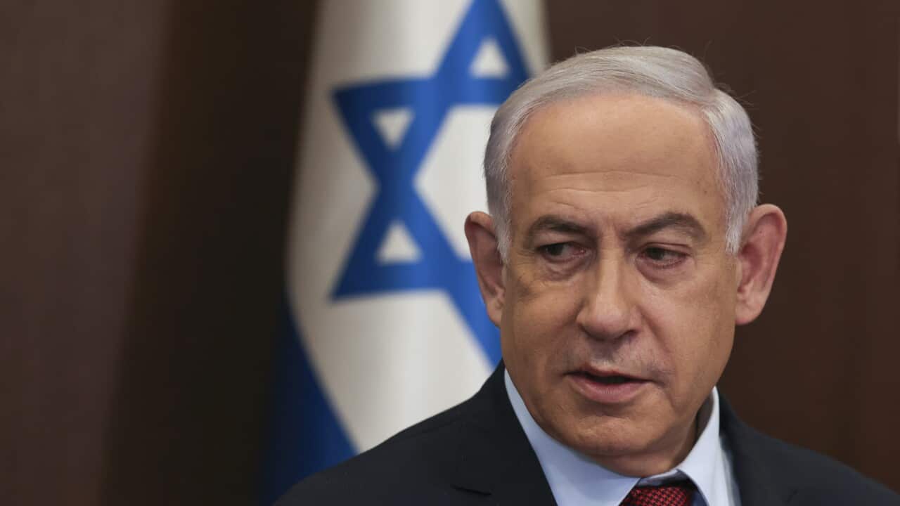 Benjamin Netanyahu standing in front of an Israeli flag