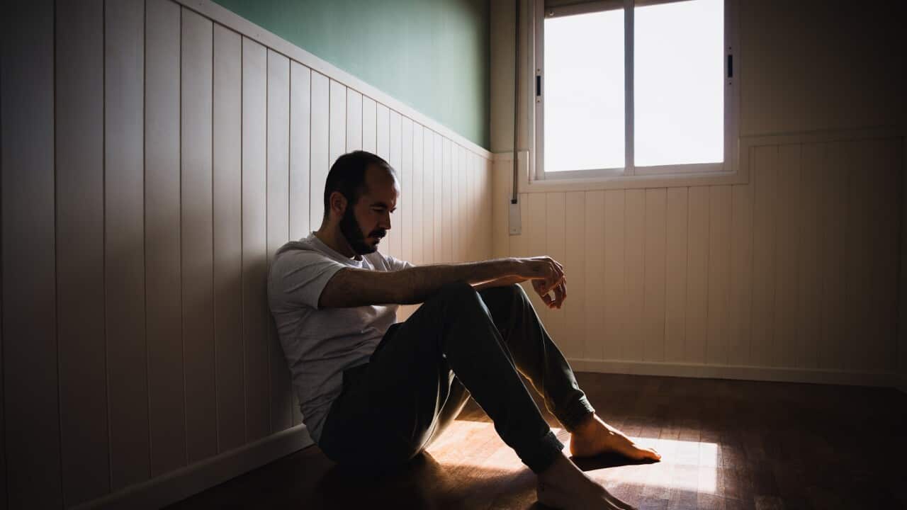 Lonely man sitting on floor by wall in dark room feeling sad
