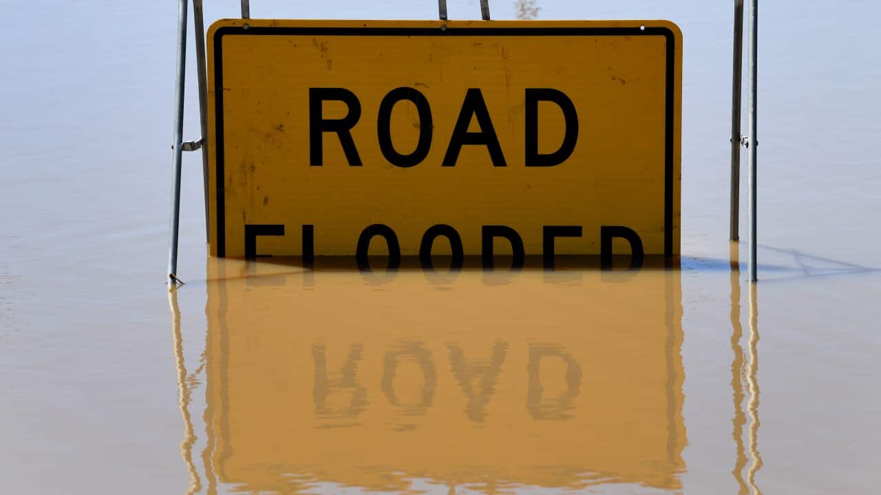 Yellow sign saying “road flooded“ partially submerged in water.