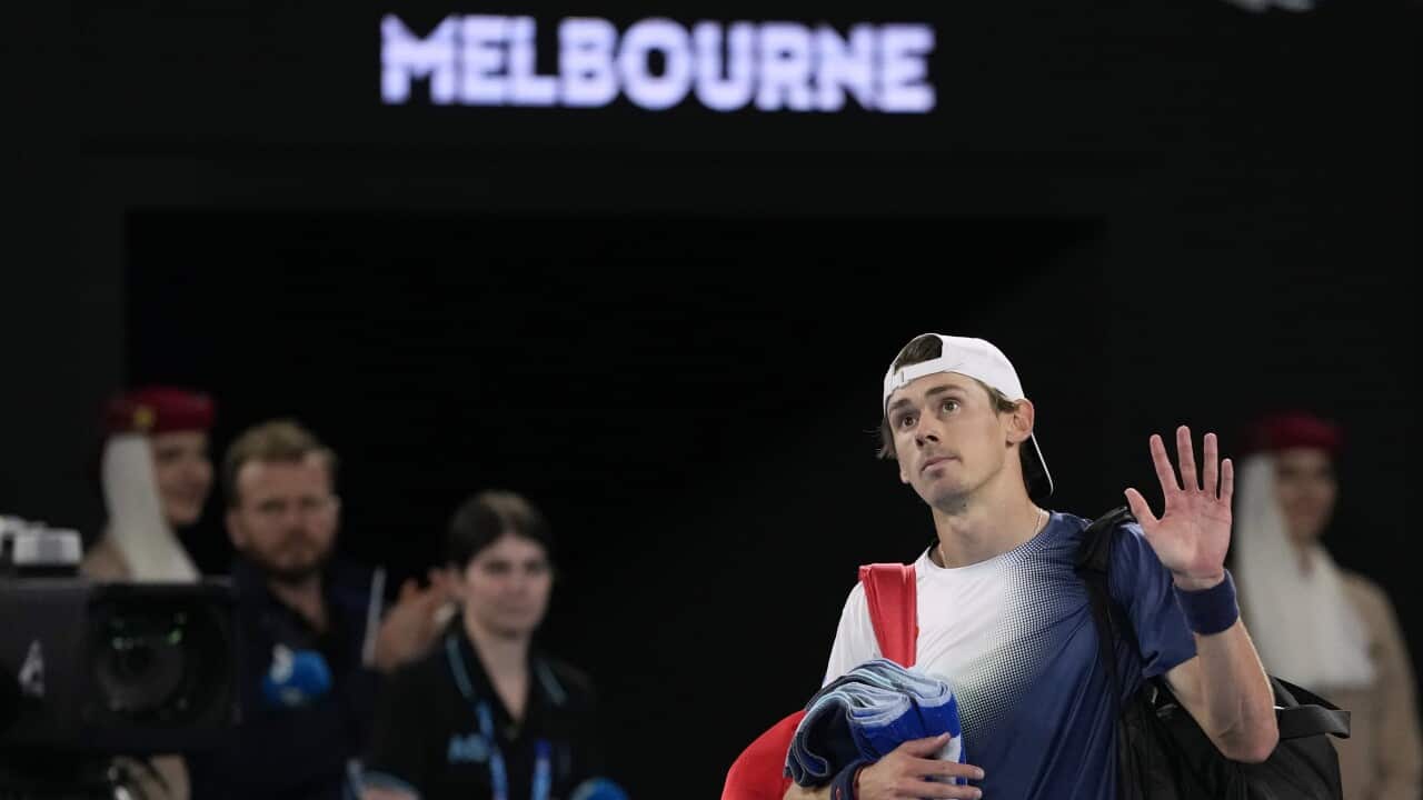 A man wearing a white cap backwards waves at a crowd after a tennis match.