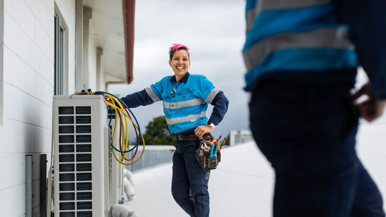 Female tradesperson on a roof working on an air-conditioning unit.
