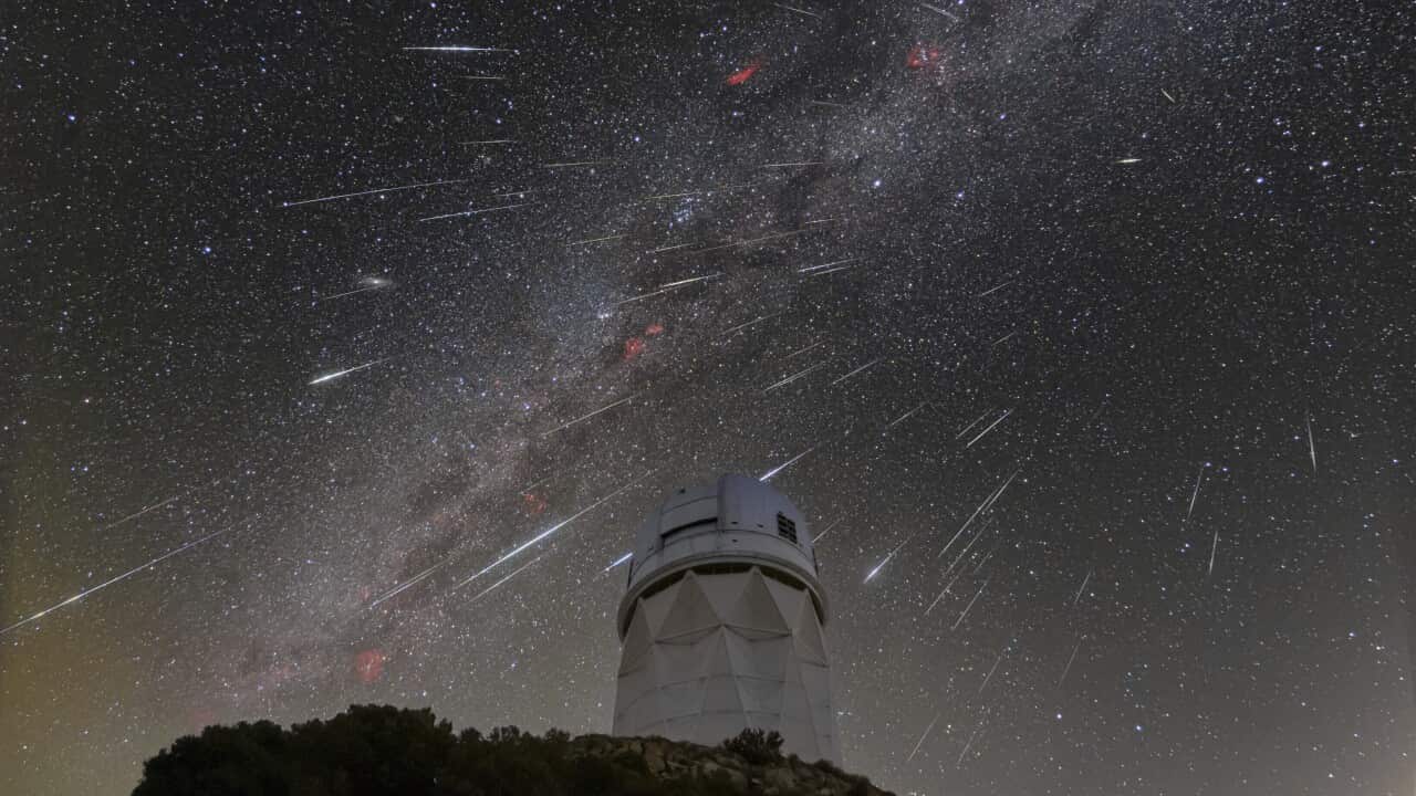 White streaks in night sky above an observatory.
