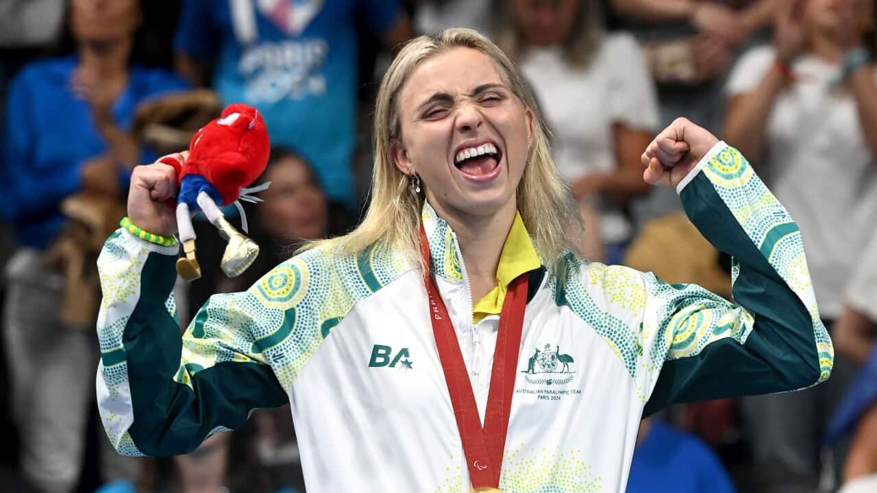 A woman smiles on a podium after winning a gold medal.