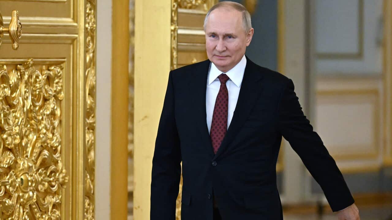 A man in black suit and red tie walks with a book in his right hand.