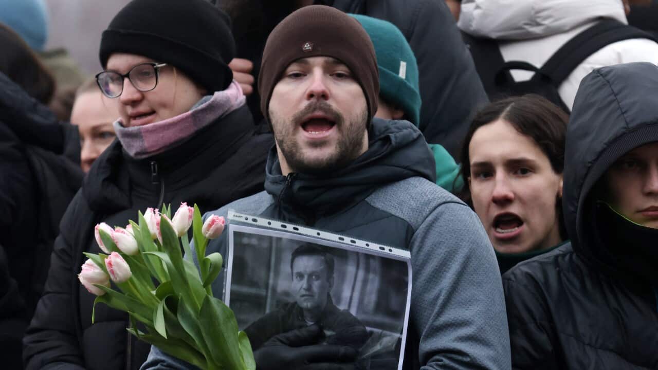 Person holding flowers and a photo of Alexei Navalny among a crowd