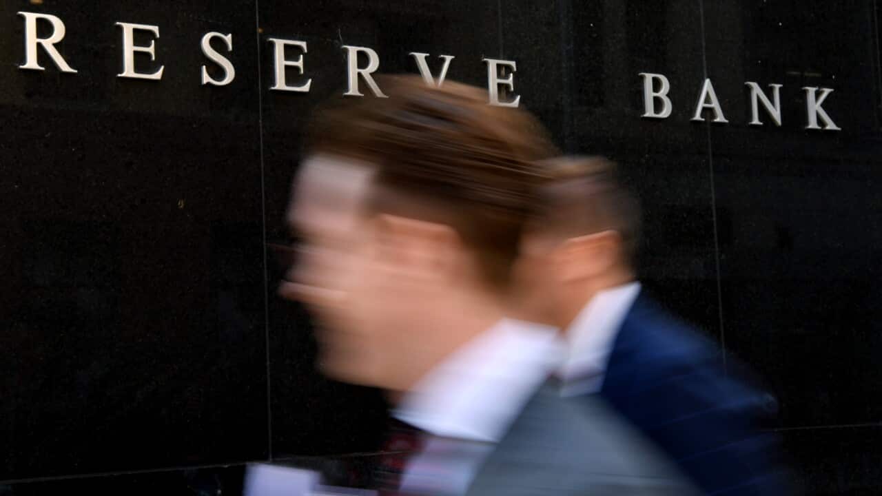 Two blurred heads walk past a sign reading Reserve Bank