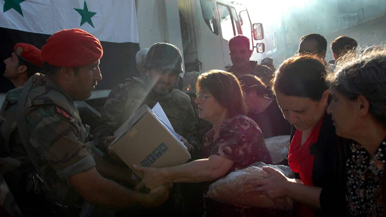 Local women receive bread and food from a Syrian soldier in Homs