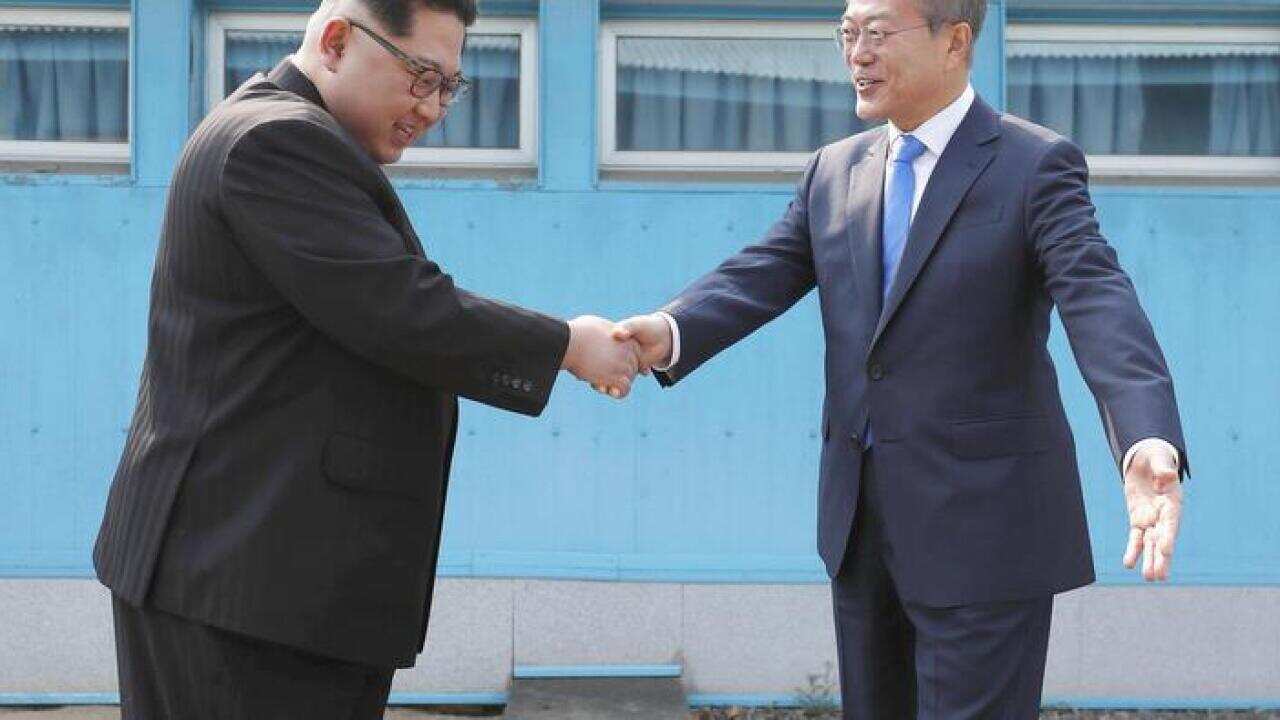 South Korean President Moon Jae In (R) and North Korean leader Kim Jong Un shake hands across the border.