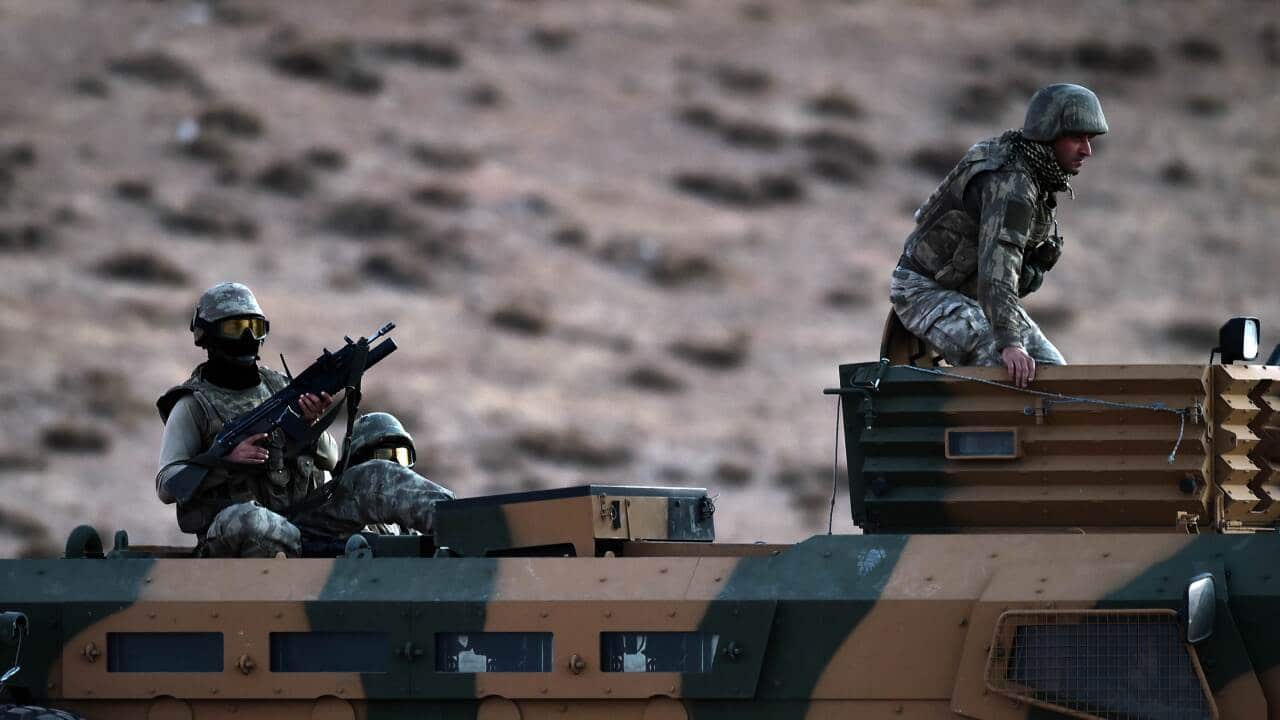 Turkish soldiers stand on an armoured vehicle at the Turkish-Syrian border