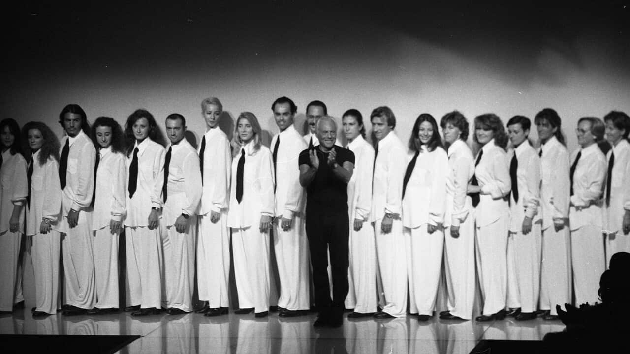 Giorgio Armani on stage clapping with models standing behind him.