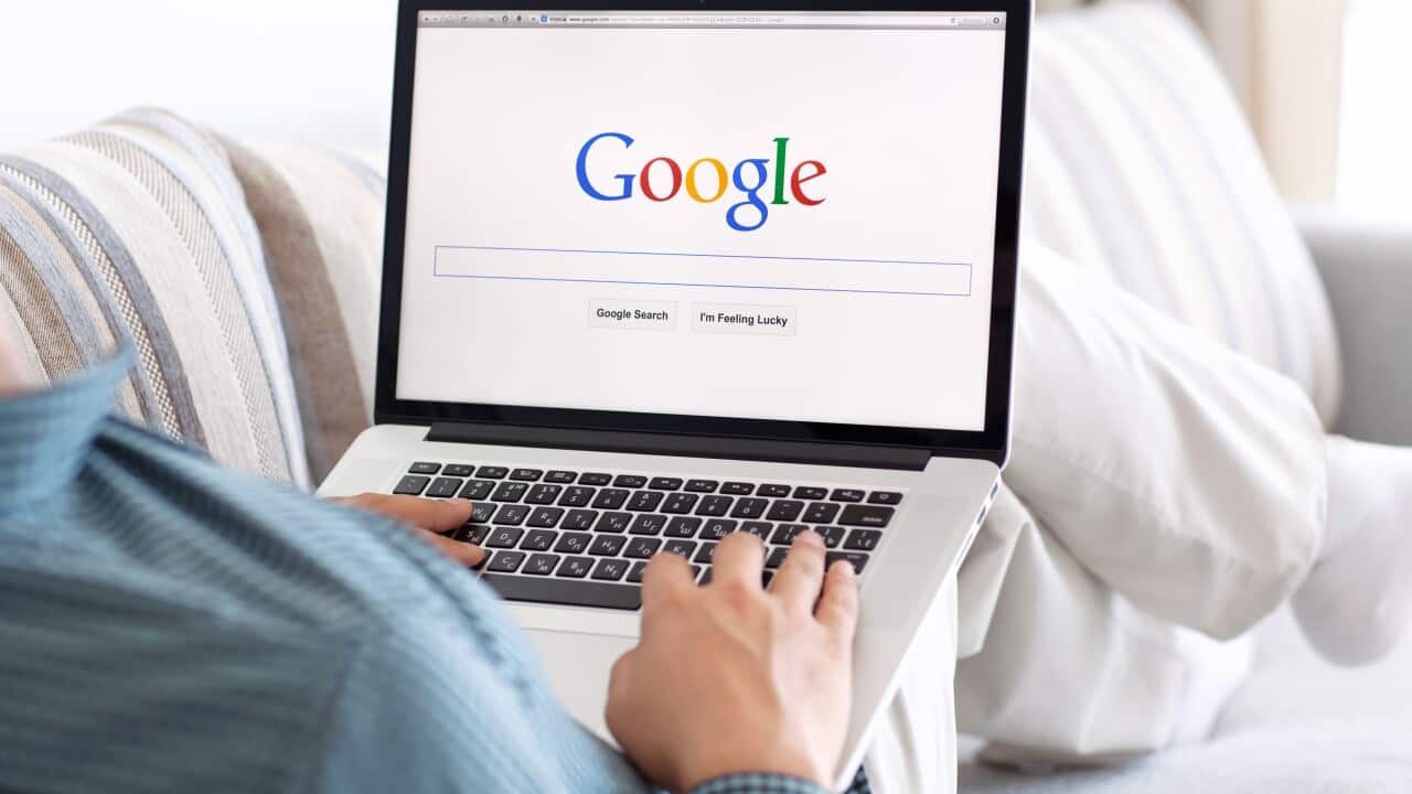 A man sitting on a couch with Google open on his laptop.