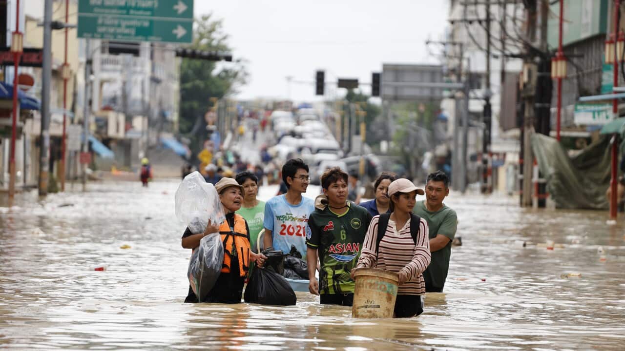 Thai residents walking through brown flood waters carrying belongings.