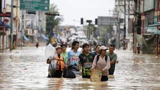 Thai residents walking through brown flood waters carrying belongings.