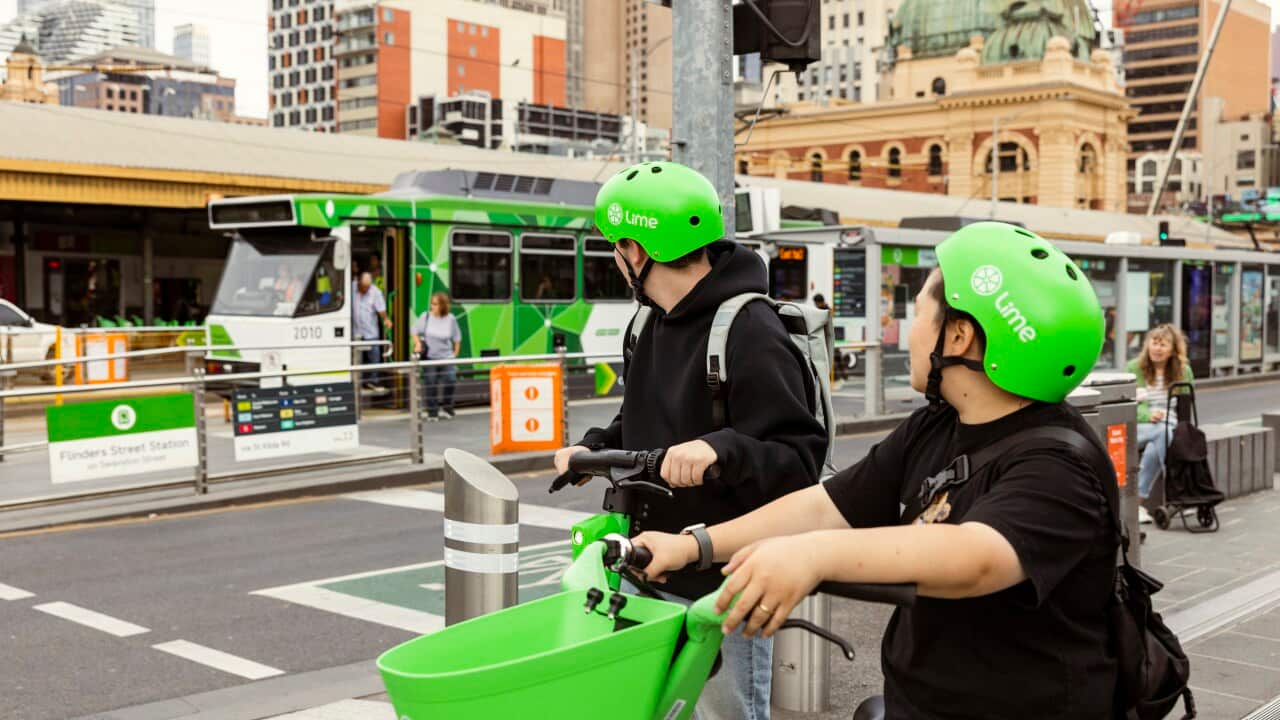 Two people in black wearing lime green helmets look across Melbourne CBD while sat on an e-bike and e-scooter.