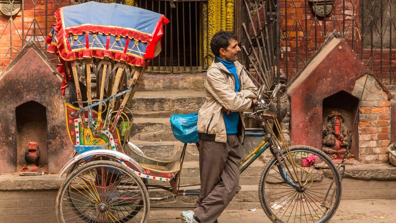 A bicycle rickshaw driver leans on his rickshaw in front of a Hindu temple while waiting for passengers. Kathmandu, Nepal