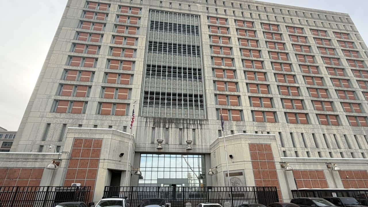Vehicles are parked outside a tall detention centre building.