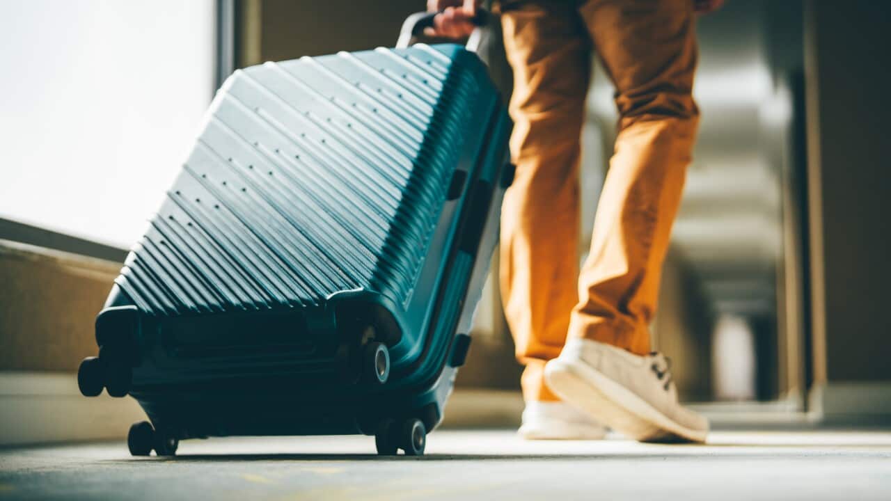 A man walks down the hotel corridor with luggage.