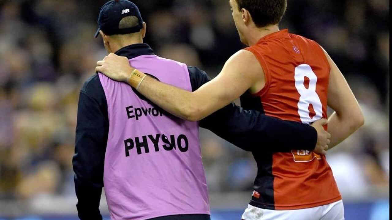 Jake Lever of the Demons is assisted off the ground.