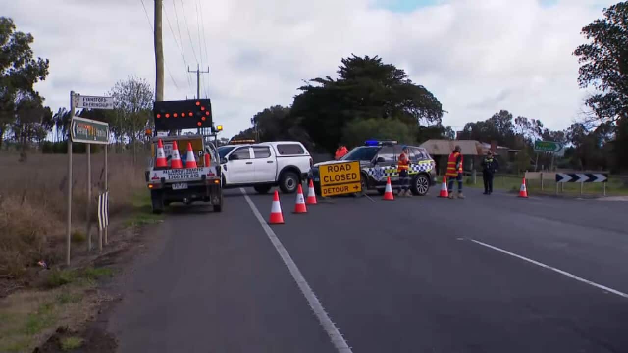 Police cars and emergency crews near a road closure sign. 