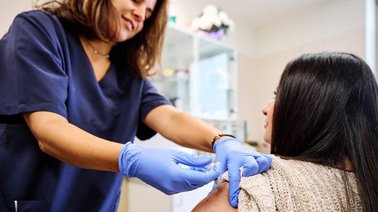 A woman in blue gloves is administering an injection into another woman's arm.