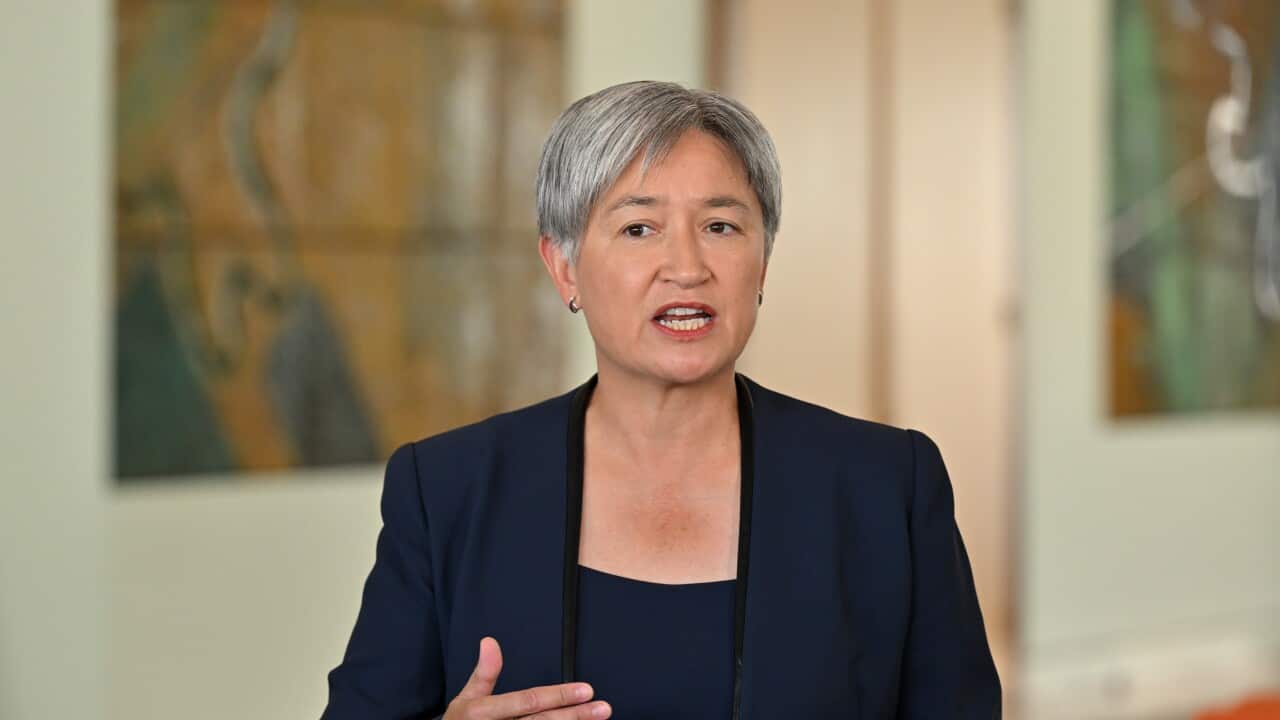 Australian Foreign Minister Penny Wong, with short grey hair and wearing a navy blue blazer, gestures with her hand while speaking in front of a blurred background.