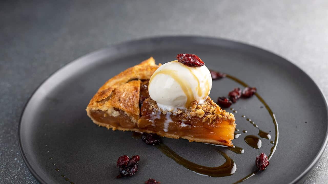 A wedge of a pastry dessert sits on a dark plate, topped with a scoop of ice-cream