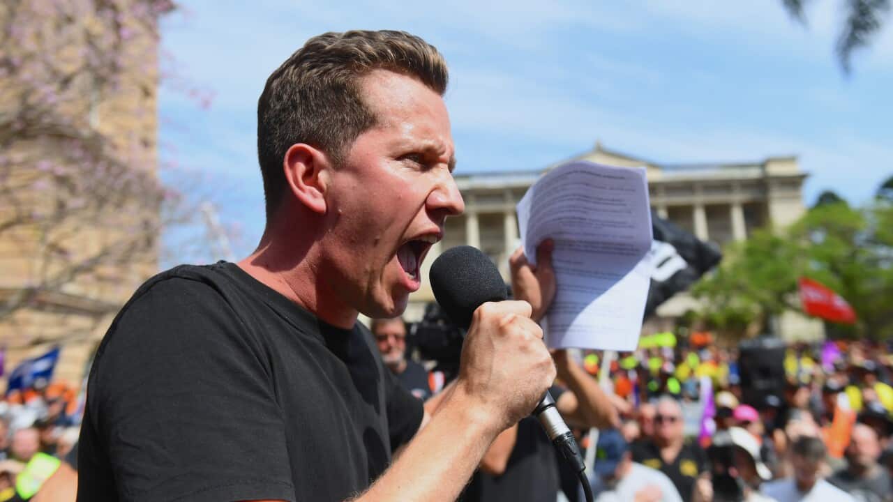 A man shouts in a microphone, holding up a piece of paper.