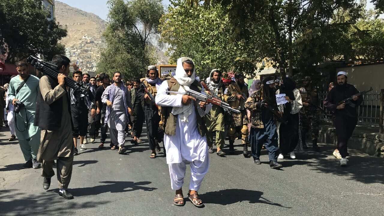 Taliban soldiers walk towards Afghans protesting in Kabul.