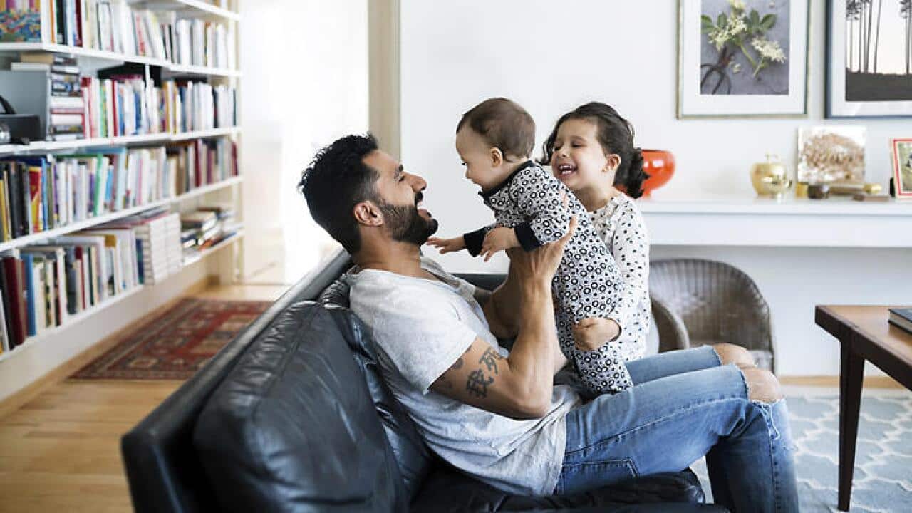 Father and daughter playing with baby girl on sofa at home
