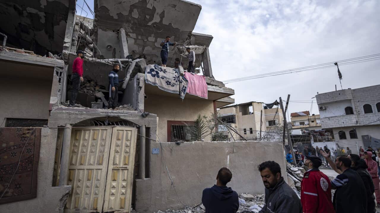 A group of people stand in front of a demolished house