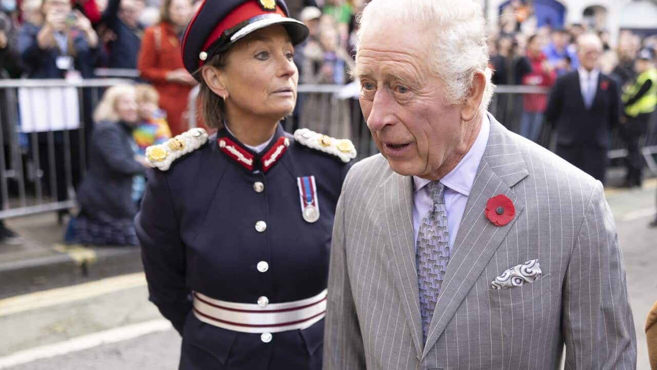 King Charles standing on a road flanked by two people.