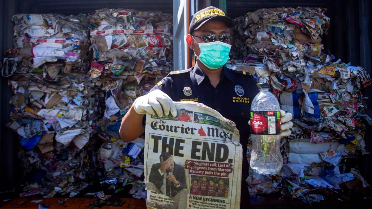 An Indonesian official holds trash as he inspects containers loaded with a combination of garbage, plastic waste and hazardous materials from Australia.