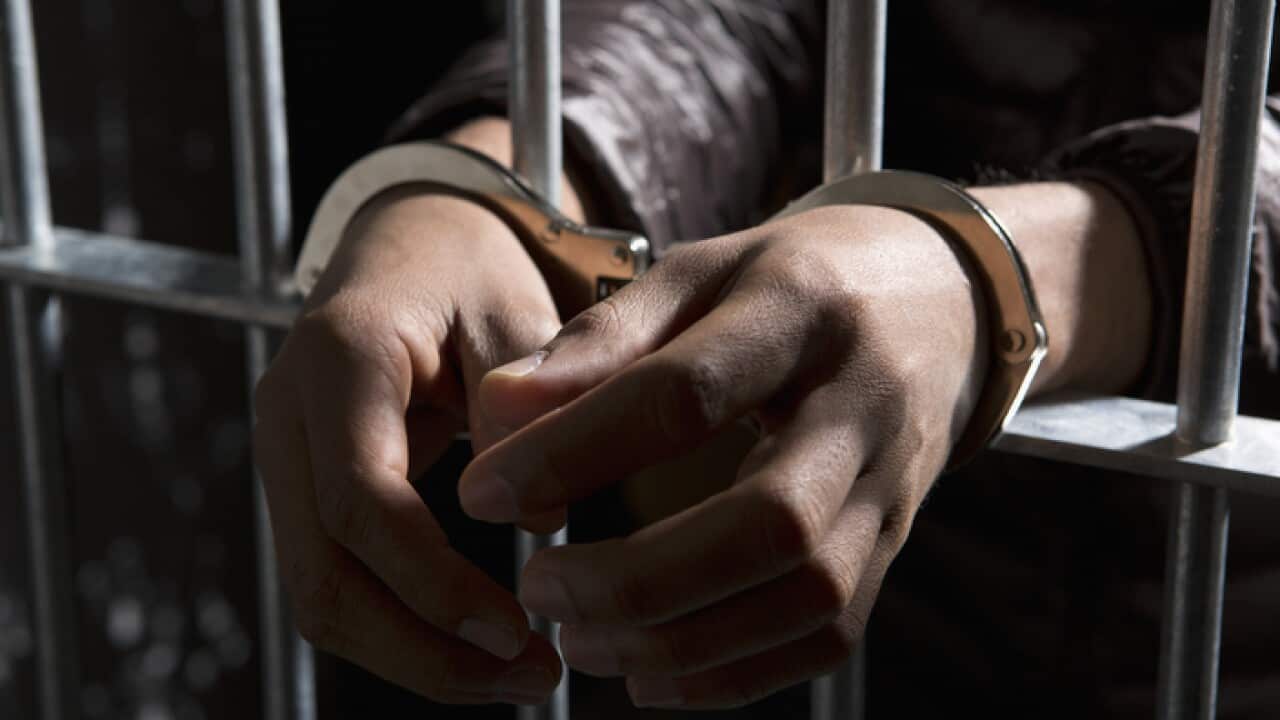 A prisoner behind bars with hands cuffed